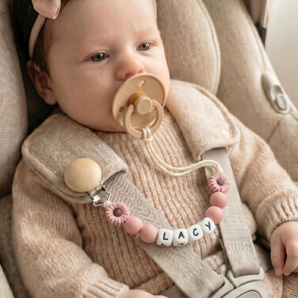 Baby in a car seat wearing a personalized daisy pacifier clip with a name in letter beads