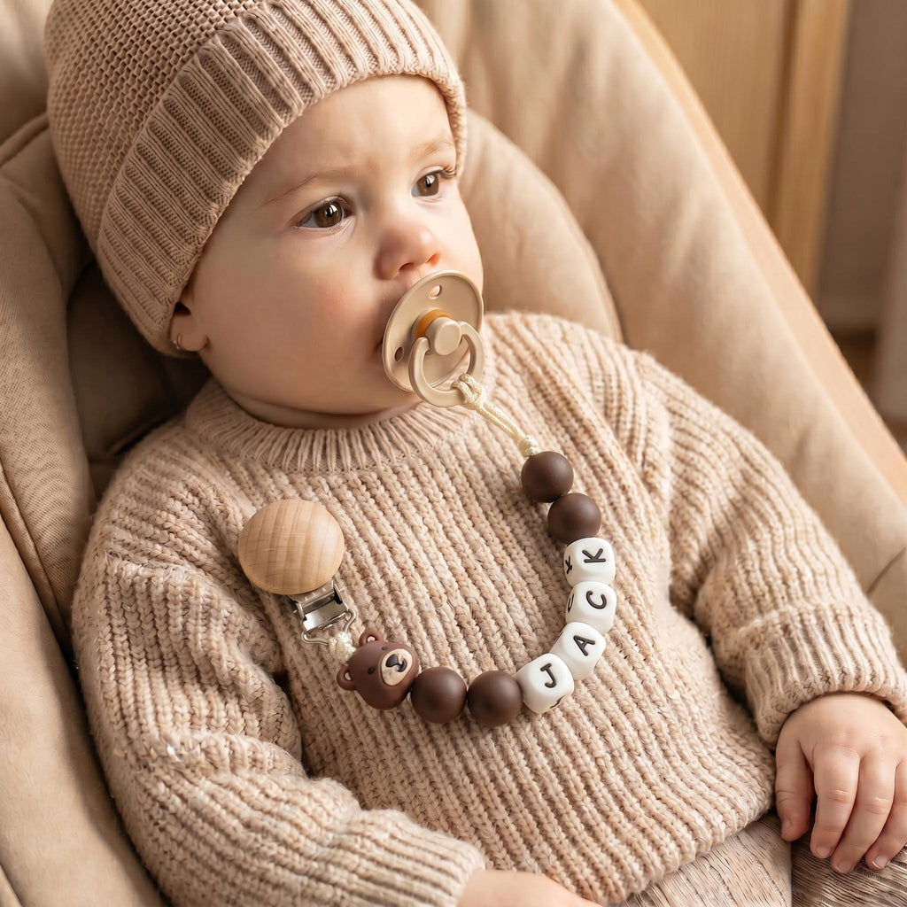 Baby wearing a personalized teddy bear pacifier clip in brown and wood beads with a name in letter beads