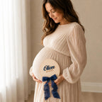 Baby name photo prop held at a maternity session, oval plaque with a navy ribbon