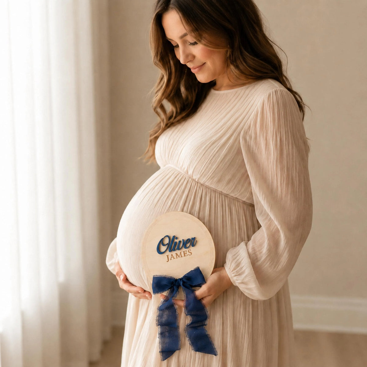 Baby name photo prop held at a maternity session, oval plaque with a navy ribbon