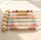 Four personalized bow pacifier clips in a flat lay, each with a baby name in letter beads and a matching bow