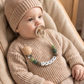 Baby wearing a personalized classic pacifier clip in sage and olive beads with a name in letter beads