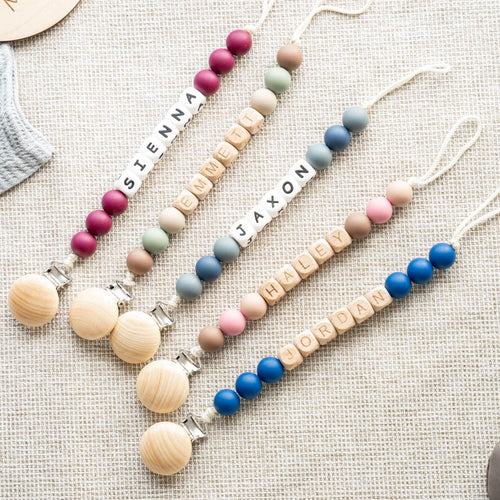 Four personalized classic pacifier clips in different bead color combinations with baby names in letter beads
