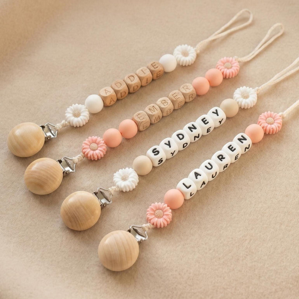 Three personalized daisy pacifier clips with baby names in letter beads and white and peach daisy beads
