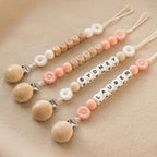 Three personalized daisy pacifier clips with baby names in letter beads and white and peach daisy beads
