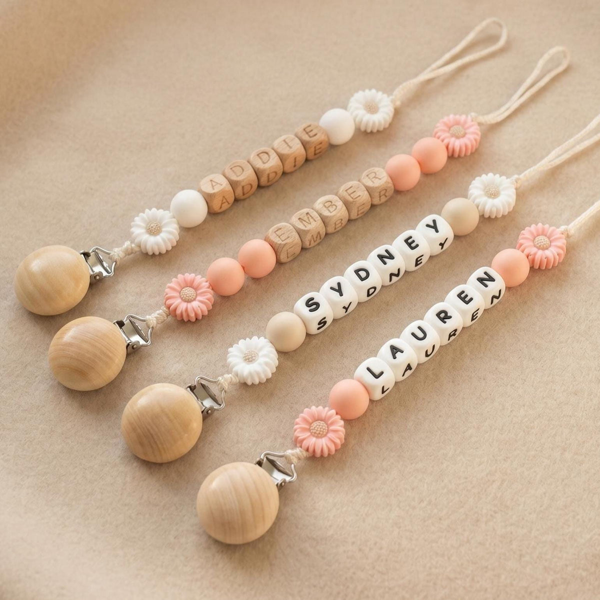 Three personalized daisy pacifier clips with baby names in letter beads and white and peach daisy beads